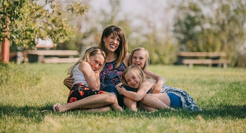woman with 3 girls sitting in a field hugging